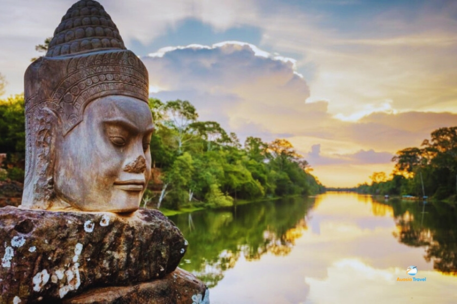 Ancient Buddha stone head by riverside at sunset in Cambodia – Auasia Travel